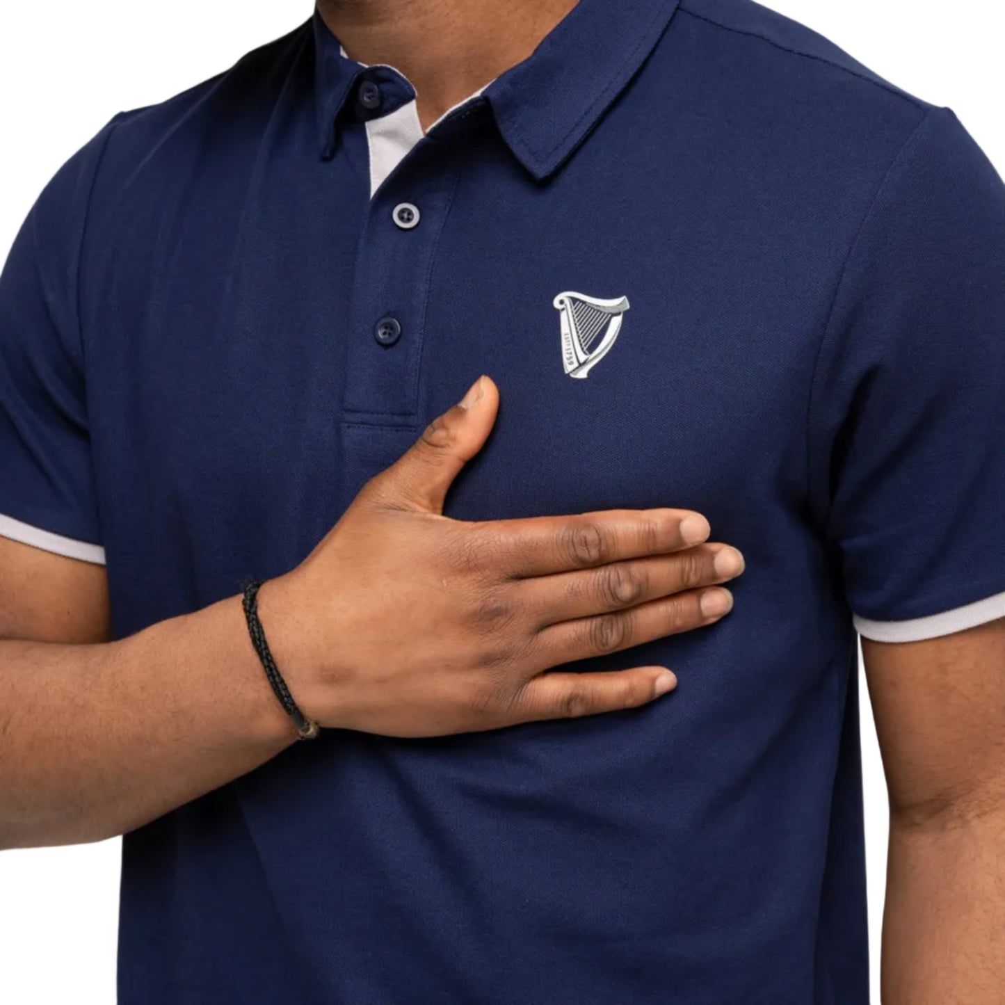 Close-up of a man holding his hand near an embroidered harp on a blue polo. 