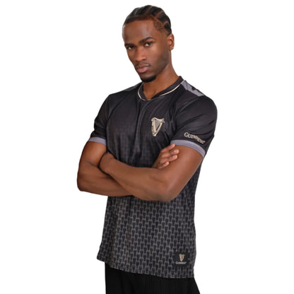 Man crossing his arms while wearing a black soccer jersey with a tiny pint glass ombre print and a harp on the left chest.