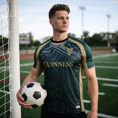 Man holding a soccer ball on a sports field wearing a jersey with Guinness branding.