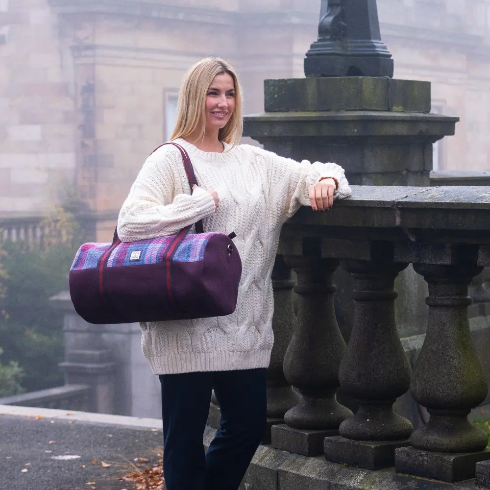 Woman holding a purple and red checkered bag in an outdoor setting with stone architecture.
