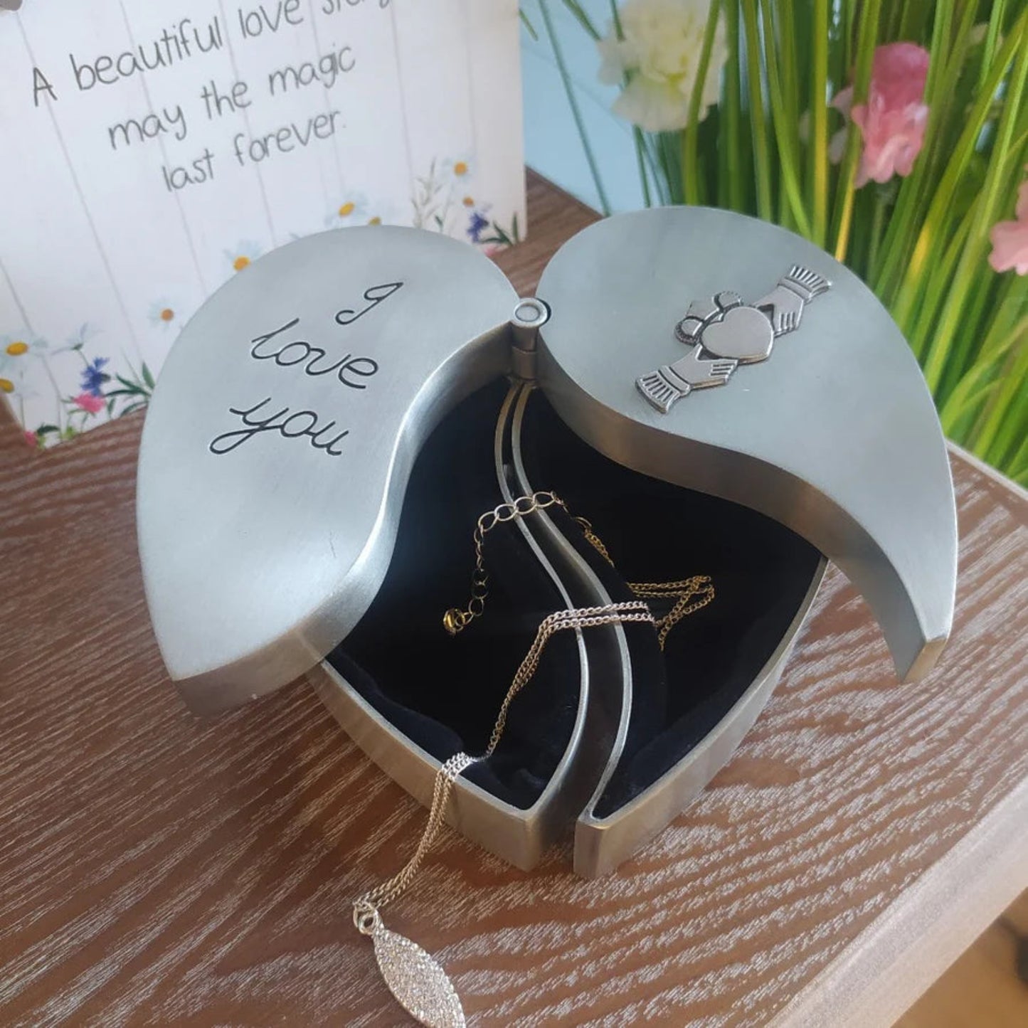 Heart-shaped jewelry box with 'I love you' engraving and gold necklaces on a wooden surface.