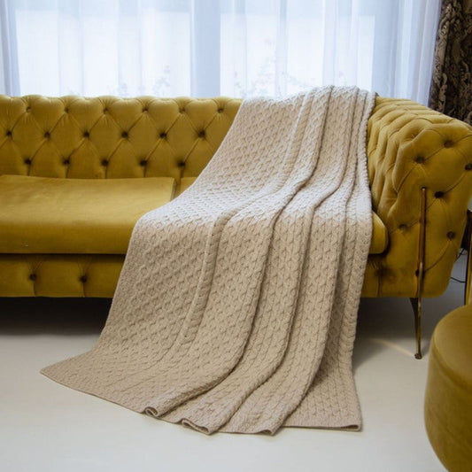 Beige blanket draped over a yellow tufted sofa with white curtains in the background