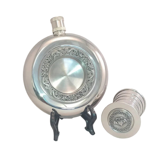 Round silver whiskey flask with a decorative Celtic-themed ring around the middle. Pewter claddagh emblem on the detachable part of it. 