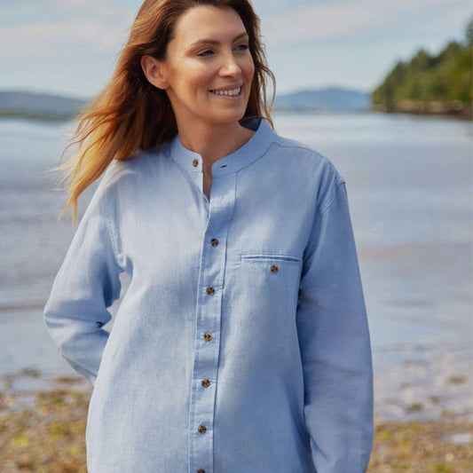 Woman wearing a light blue shirt by a lake with mountains in the background