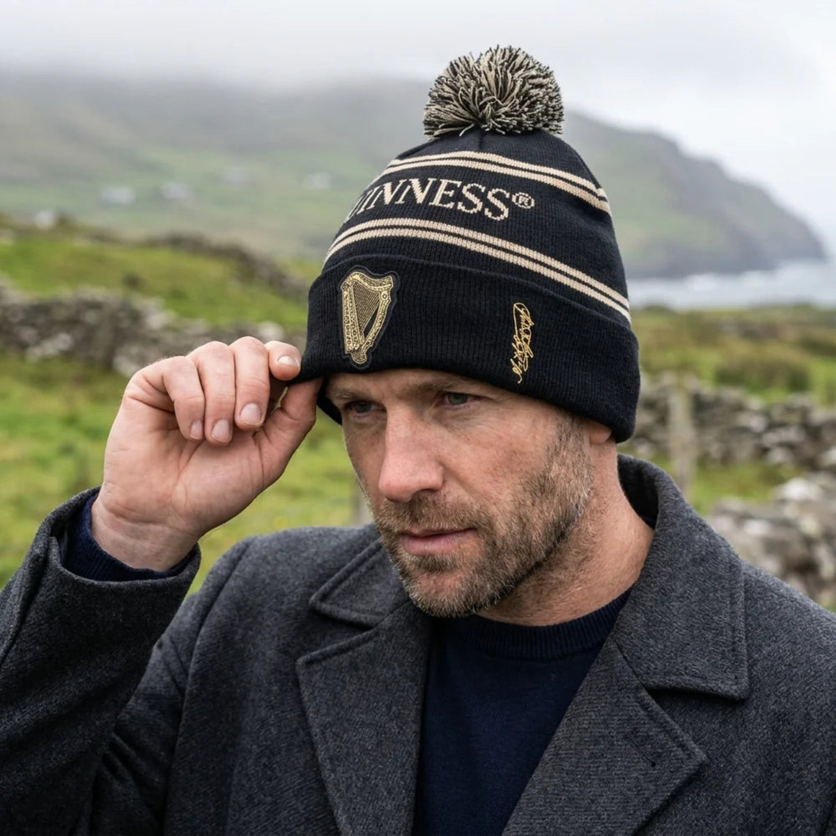 Man wearing a Guinness beanie in a scenic outdoor setting