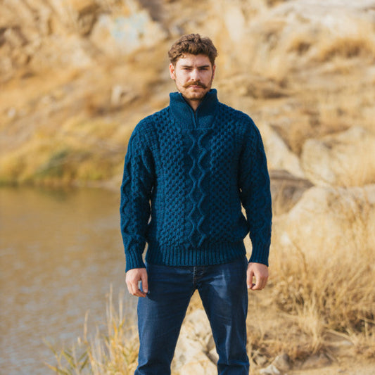 A man standing outdoors wearing a blue merino wool half zip sweater with geometric pattern and a visible zipper.