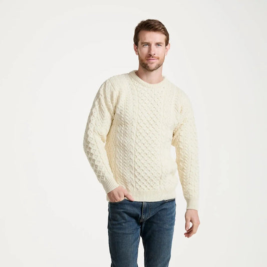 Man wearing a cream sweater and blue jeans on a white background