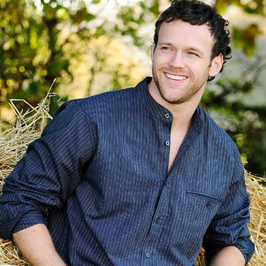 Man wearing a blue shirt and jeans standing on hay with a blurred natural background