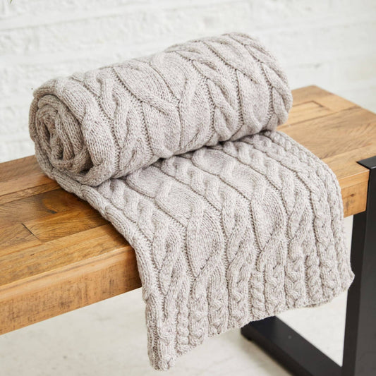 Rolled and draped textured blanket on a wooden bench against a white brick wall.