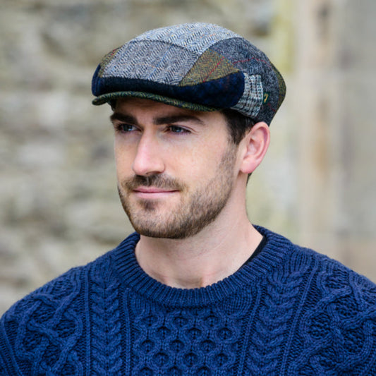 Man wearing a blue knitted sweater and patterned cap against a stone wall background