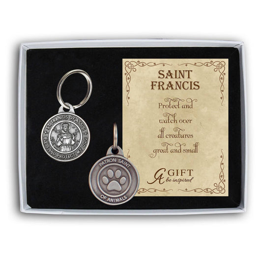 Two silver keychains in a box with a card about Saint Francis on a white background