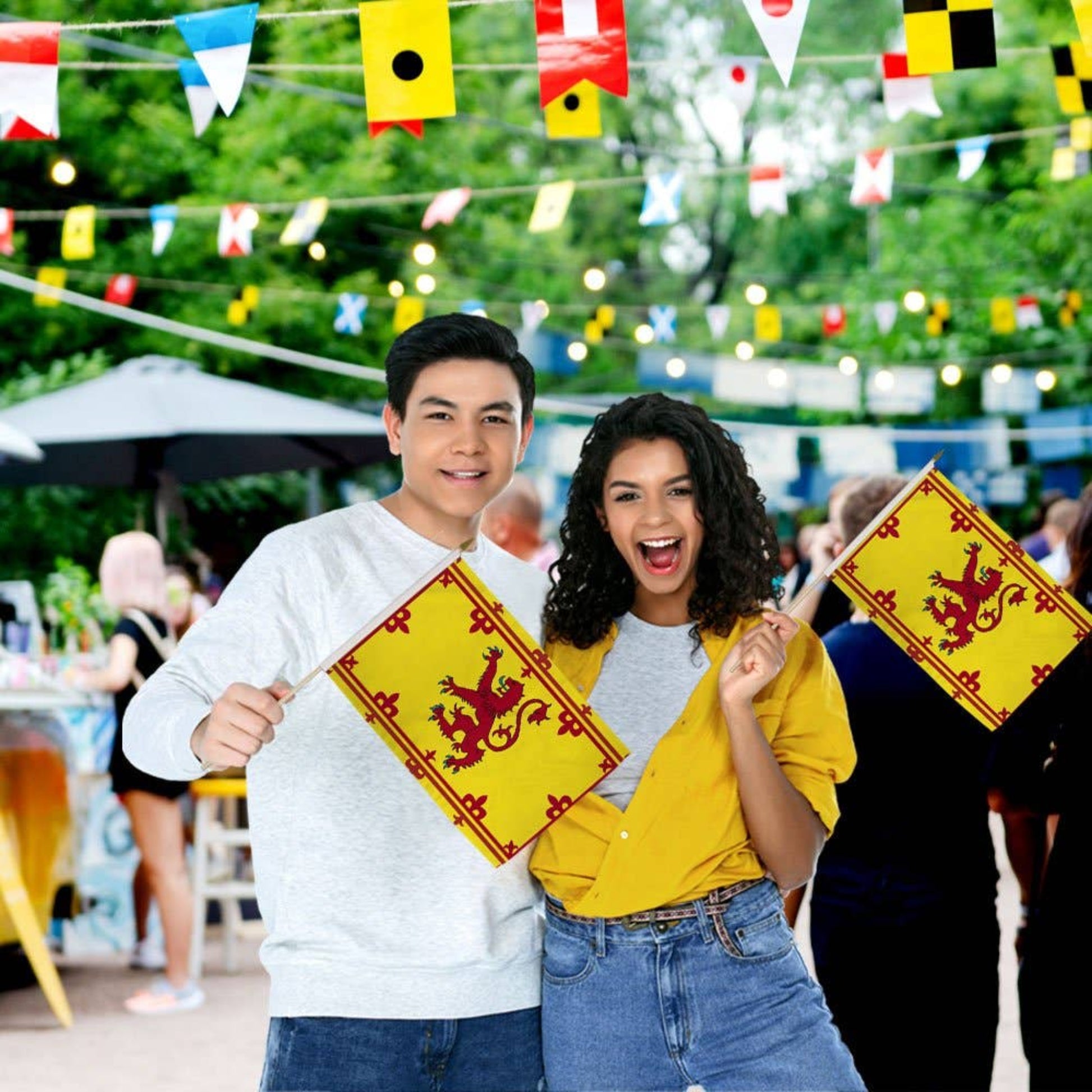 Two people holding yellow flags with red lions at an outdoor event.