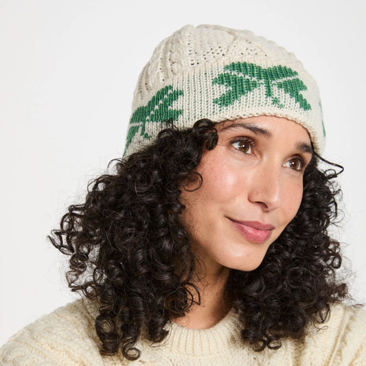 Woman wearing a cream knit sweater and a matching knit hat with green leaf patterns on a white background