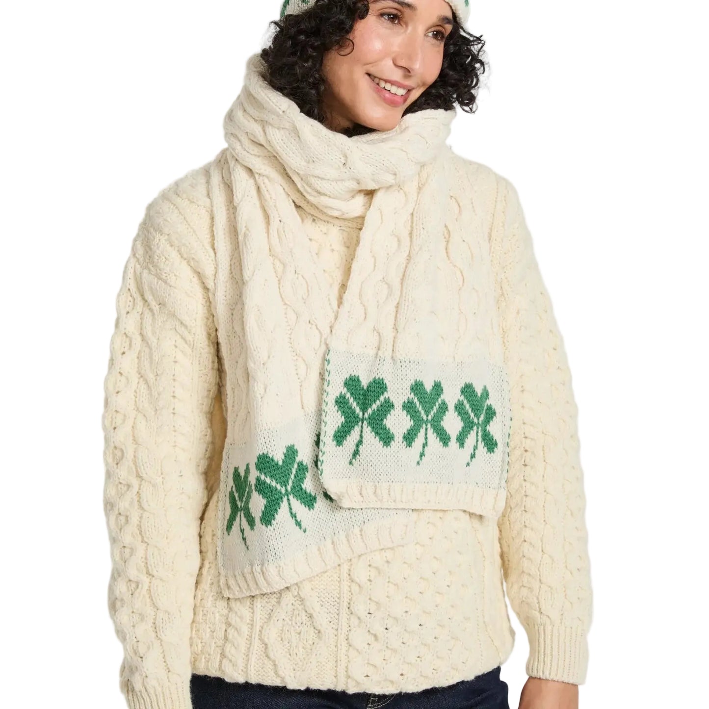 Woman wearing a cream cable knit sweater with green shamrock design and matching scarf on a white background