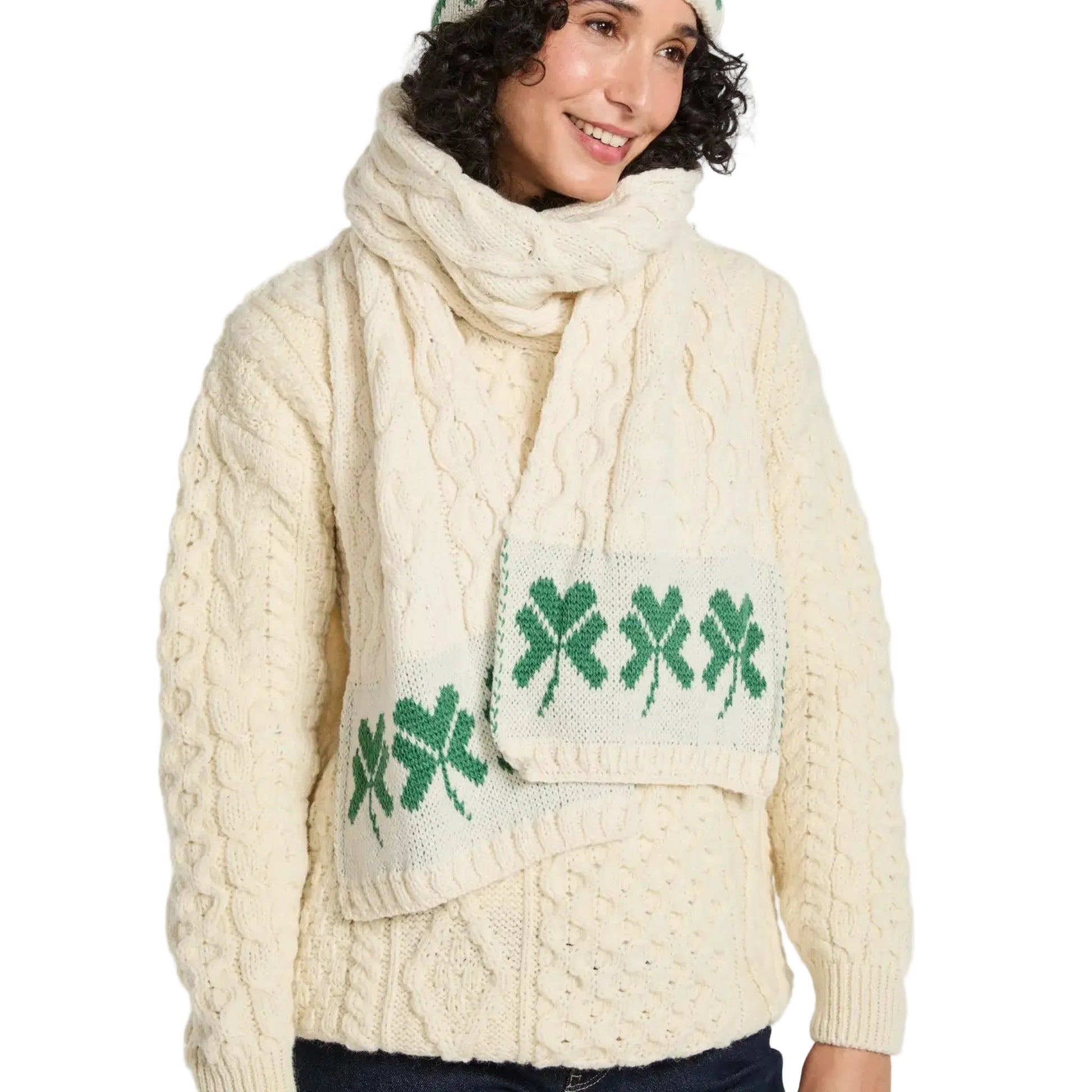 Woman wearing a cream cable knit sweater with green shamrock design and matching scarf on a white background