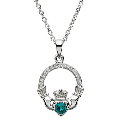 Silver claddagh pendant encrusted with white gems. The heart in the center contains one larger teal gem. 