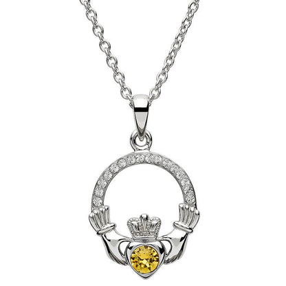 Silver claddagh pendant encrusted with white gems. The heart in the center contains one larger light orange gem. 