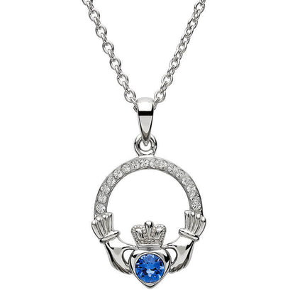 Silver claddagh pendant encrusted with white gems. The heart in the center contains one larger blue gem. 