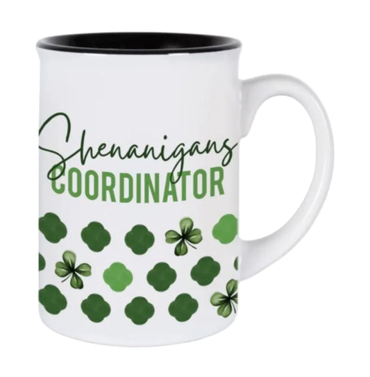 A white ceramic mug with green text reading 'Shenanigans Coordinator' and green clover patterns.