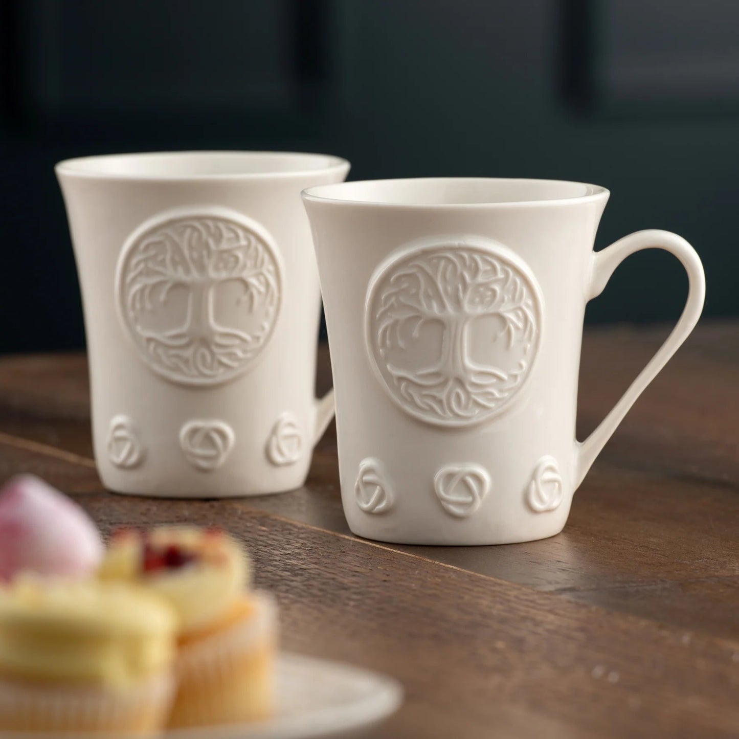 Two white porcelain mugs with tree of life designs on a wooden surface.