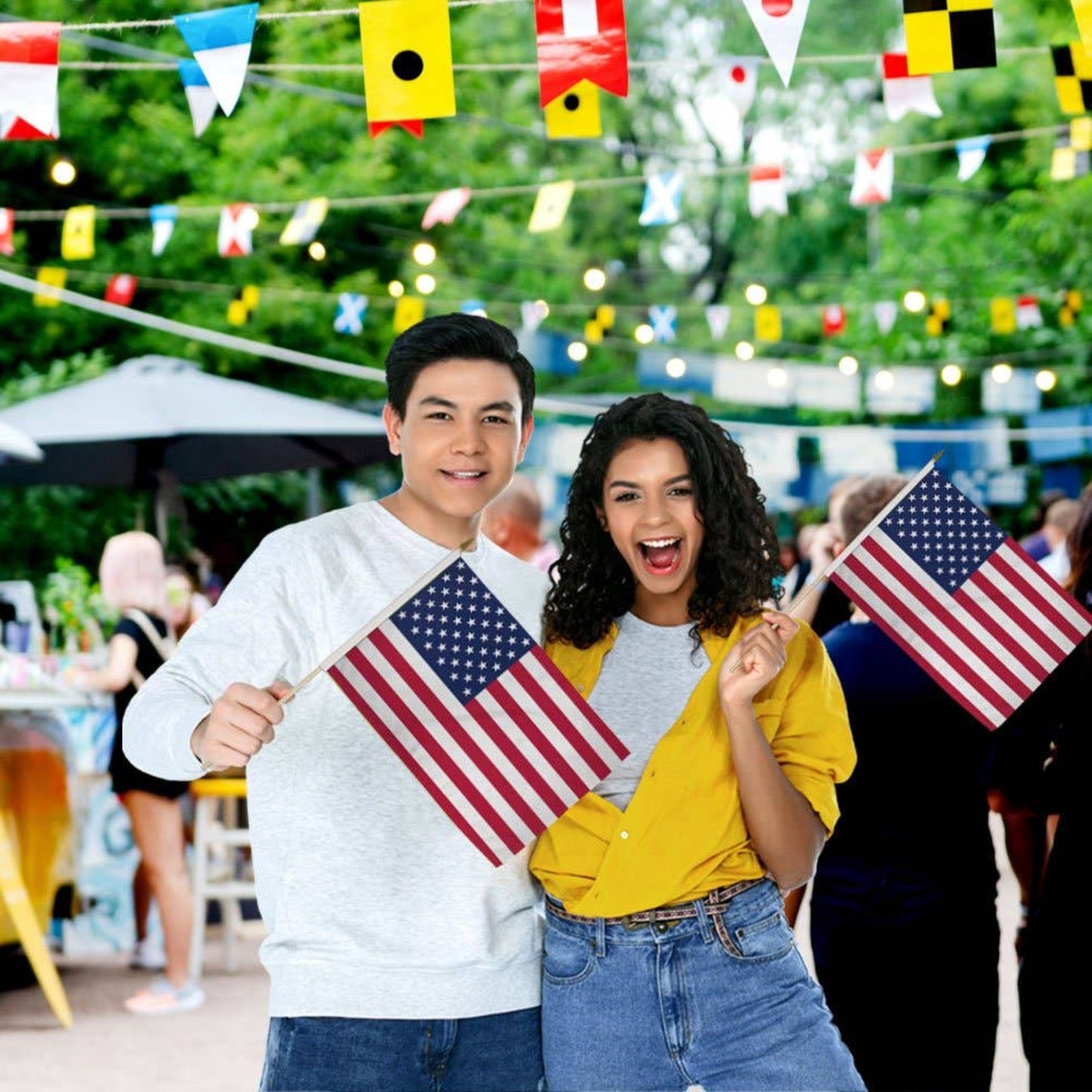 Two people holding American flags in a festive outdoor setting.