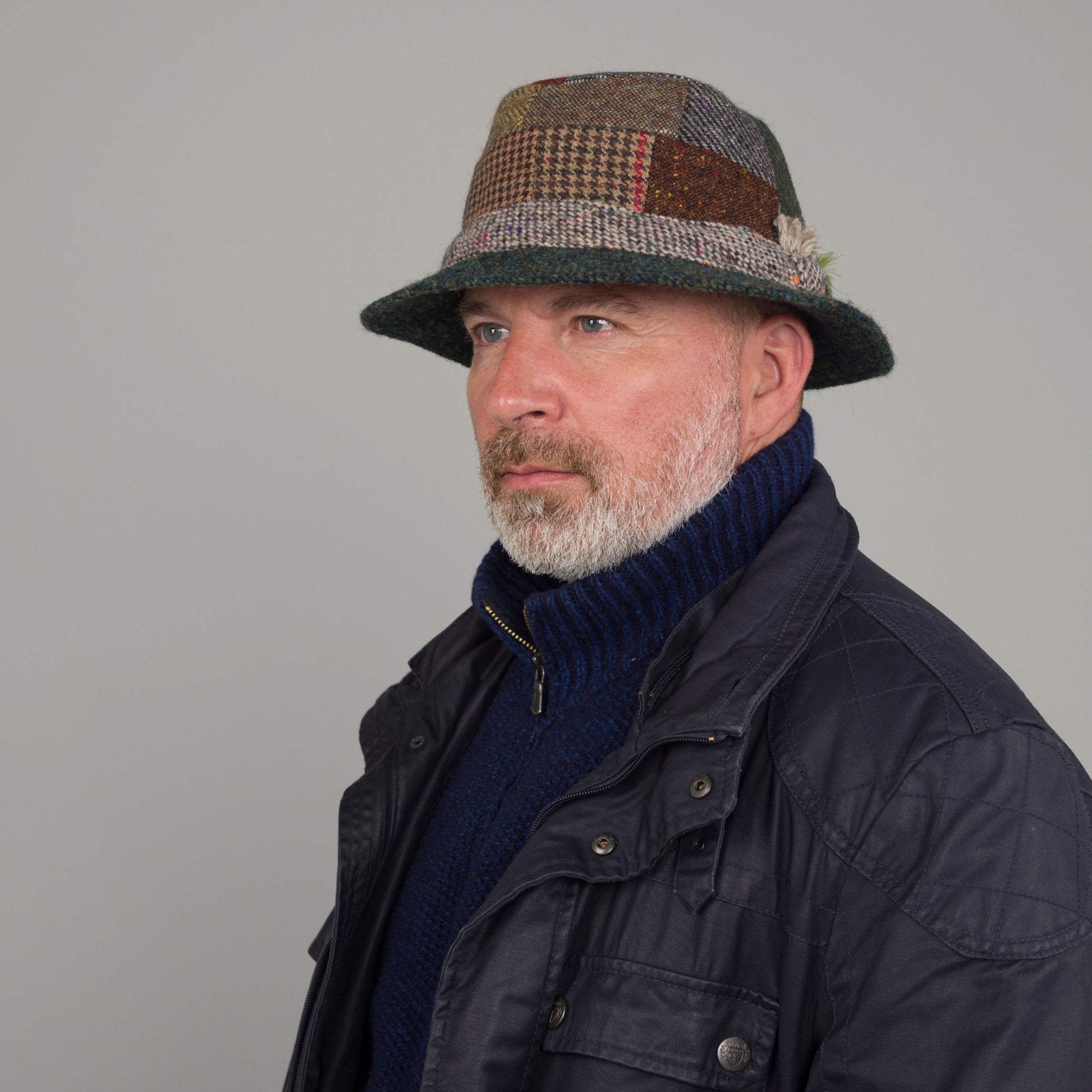 Man wearing a patchwork hat and dark jacket against a gray background