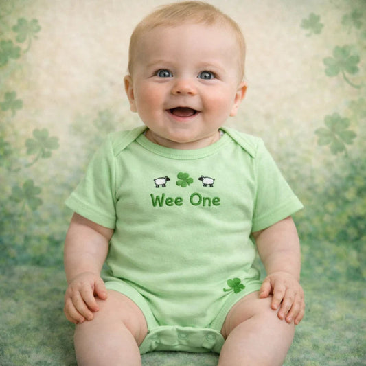 Baby wearing a green onesie with 'Wee One' text and shamrock designs on a shamrock patterned background.