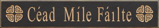 Decorative sign with 'Cáid Móile Fáilte' in gold on a black background