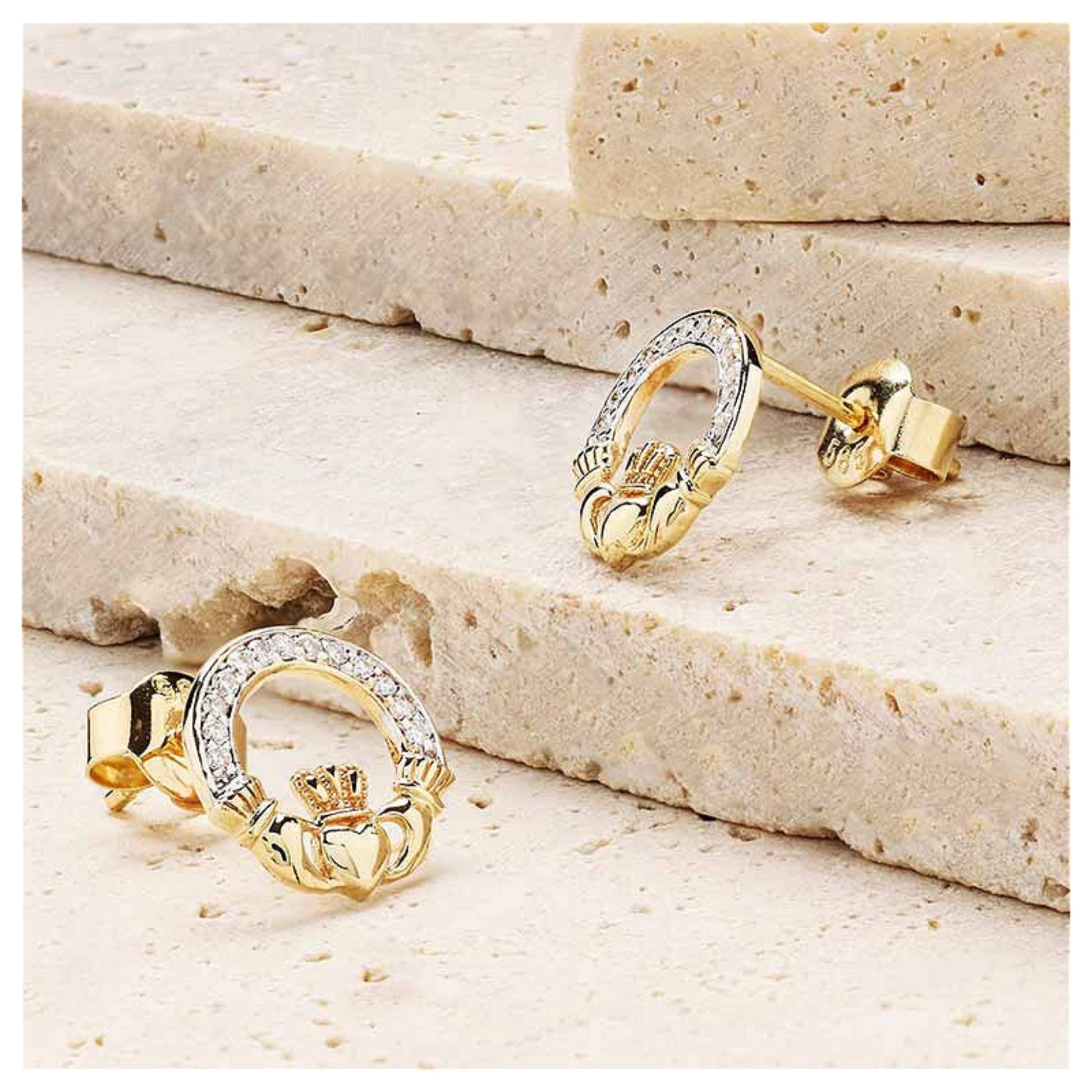 Gold claddagh earrings resting on a marble surface.