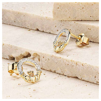 Gold claddagh earrings resting on a marble surface.