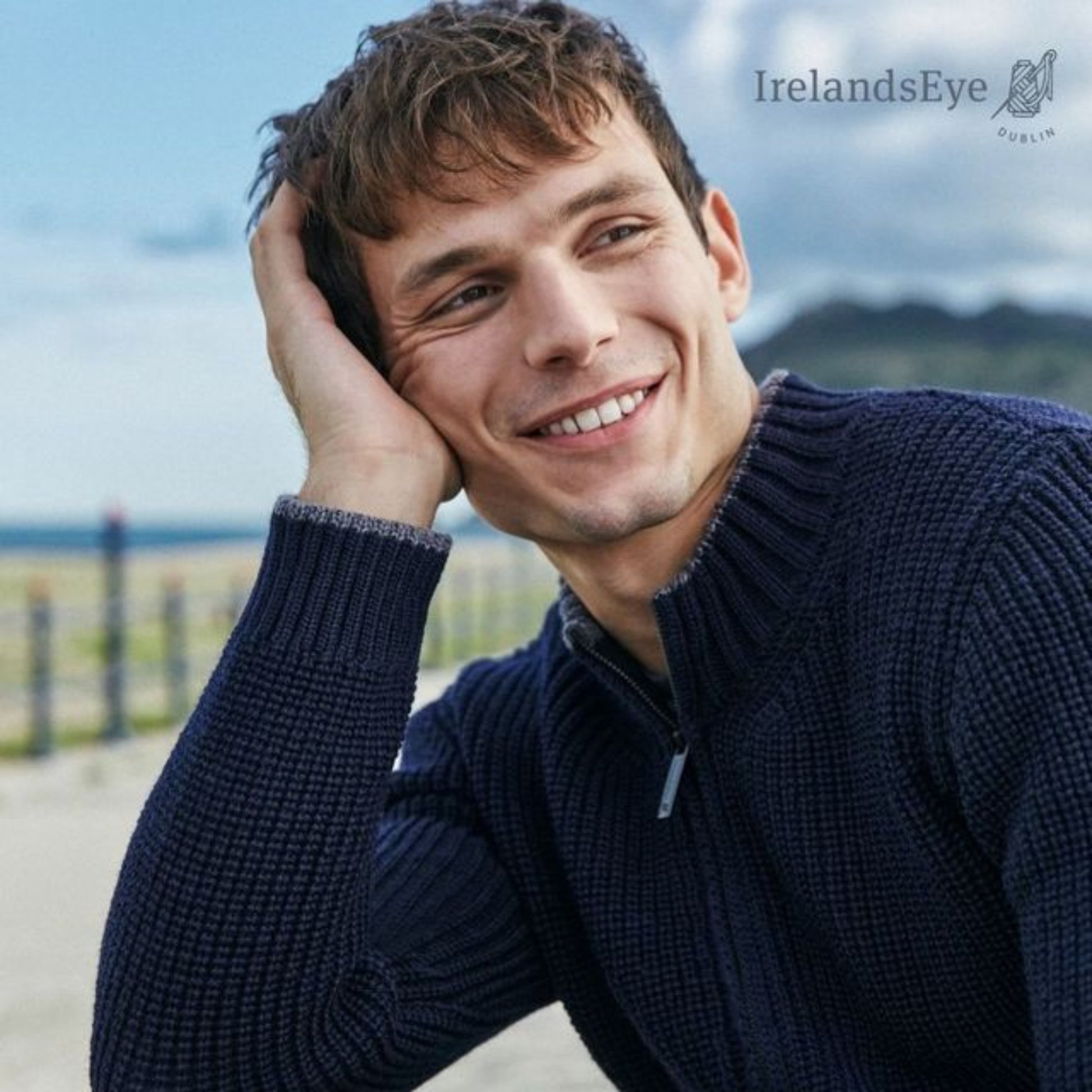Man wearing a navy sweater sitting outdoors with 'Ireland's Eye' logo in the corner.