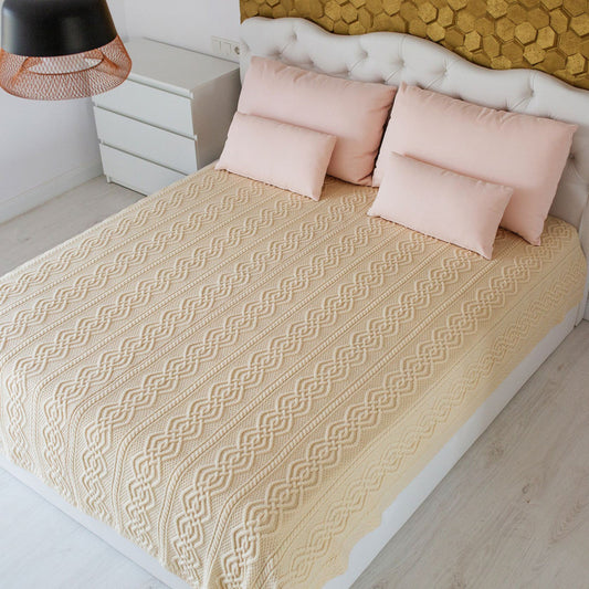 Beige knitted blanket on a bed with pink pillows in a bedroom setting.
