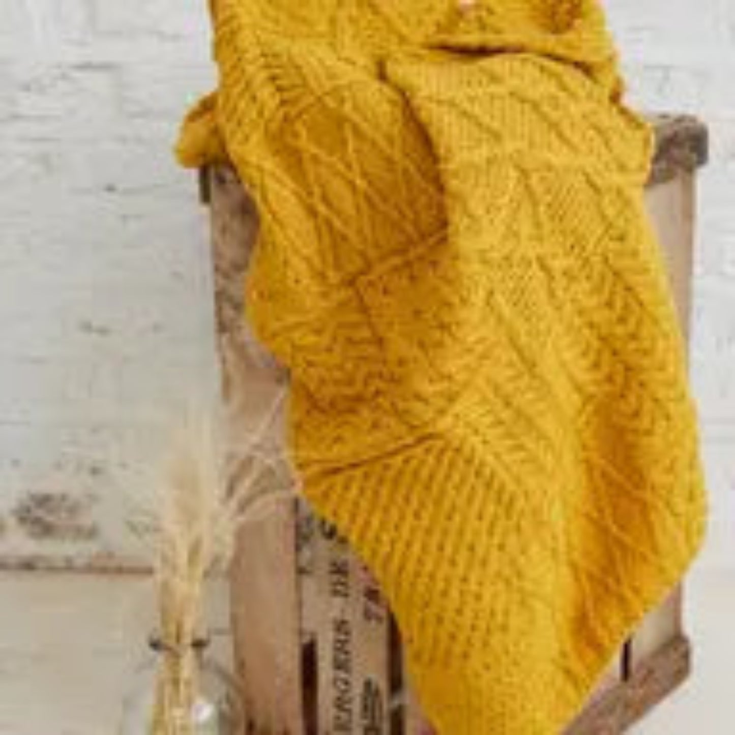 Mustard yellow knitted blanket draped over a chair on a wooden floor.