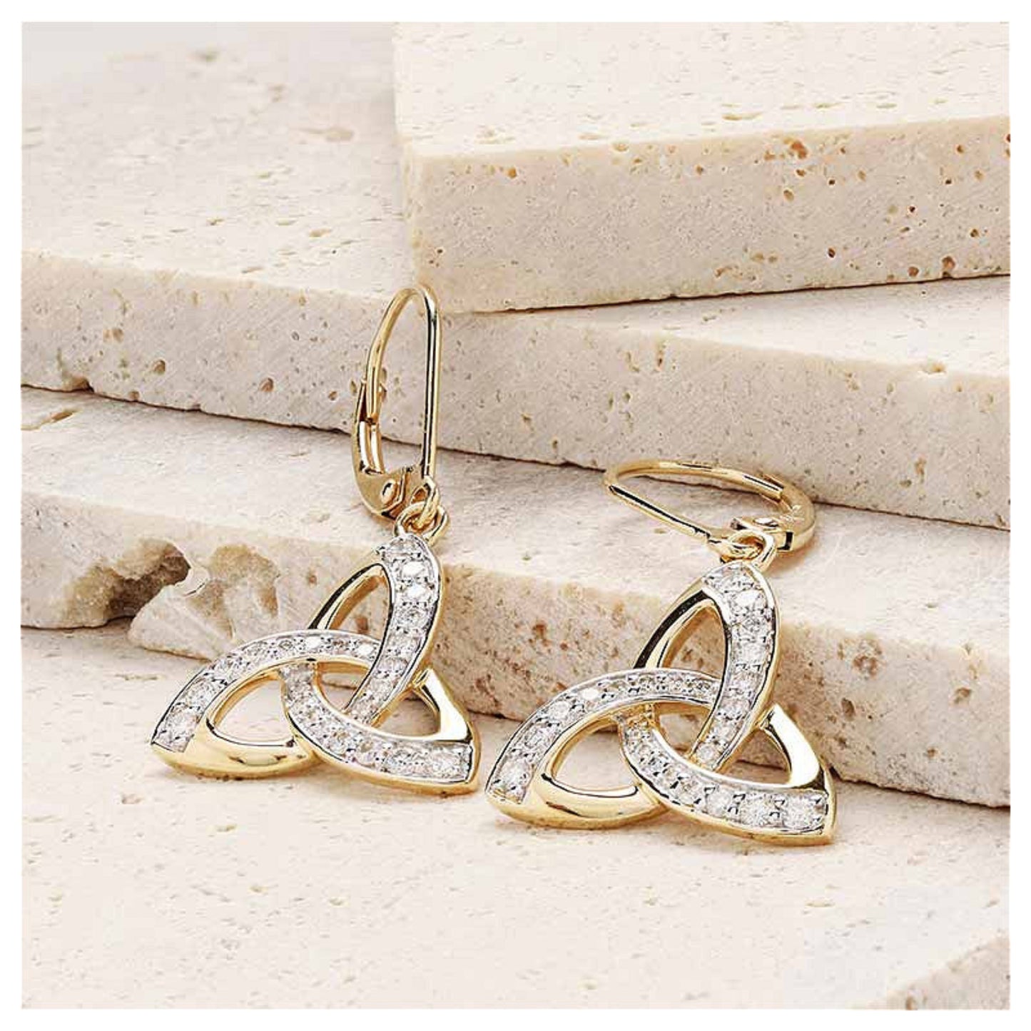 Gold trinity knot earrings resting on a marble surface.