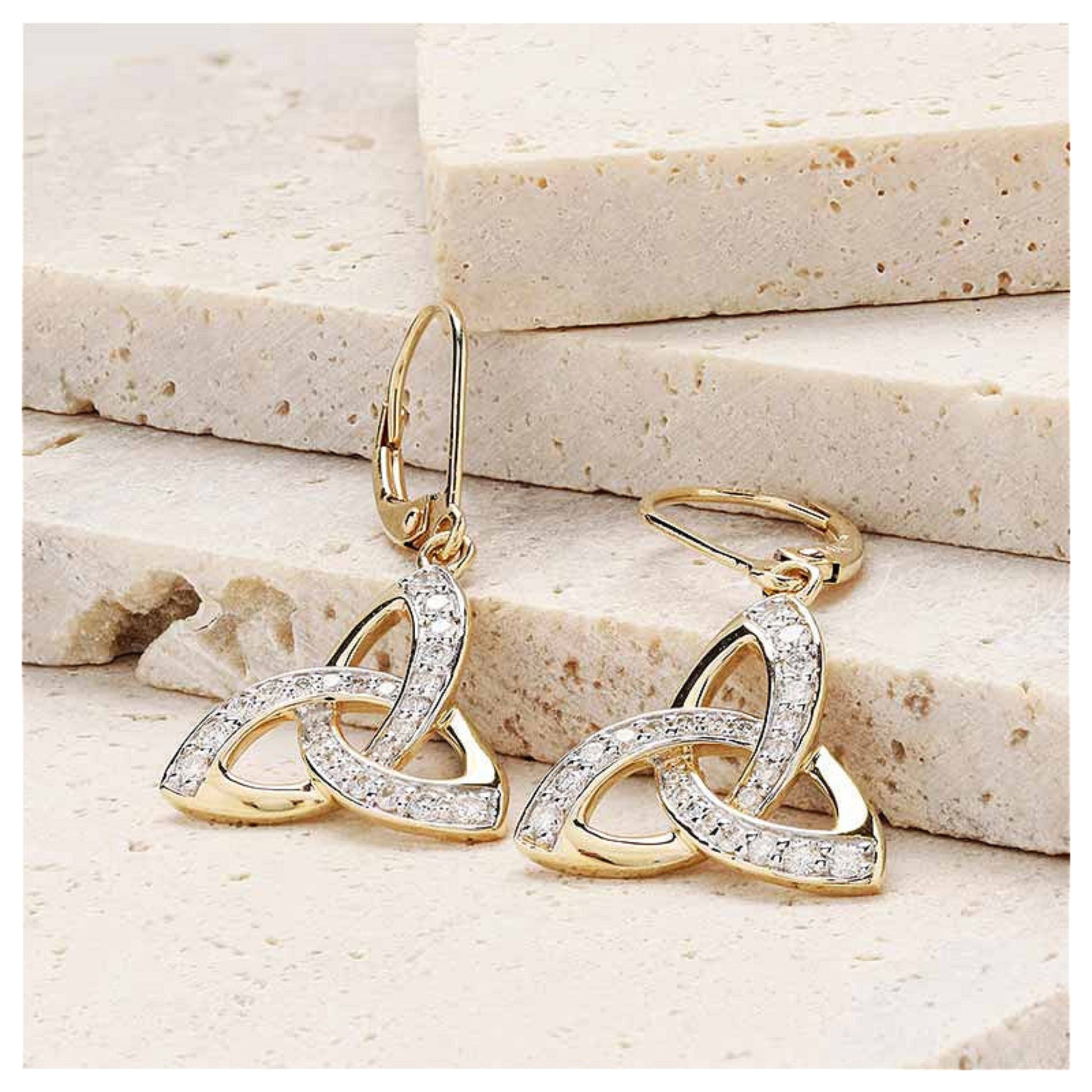 Gold trinity knot earrings resting on a marble surface.