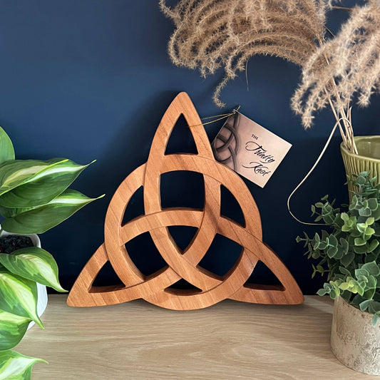 Wooden trinity knot decoration on a wooden surface with plants and a dark blue wall in the background.